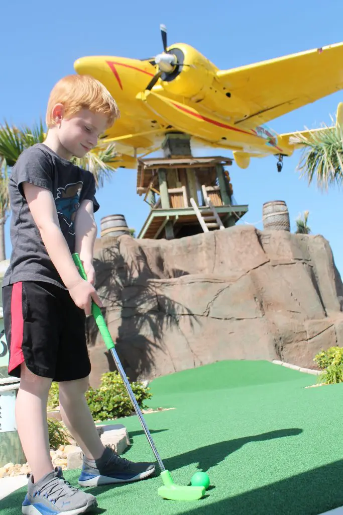 kid at mini golf with plane in the back